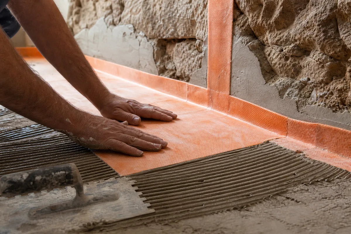 Artisan appliquant une natte d’étanchéité au sol d’une future douche à l’italienne